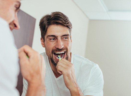 Man smiling while brushing his teeth
