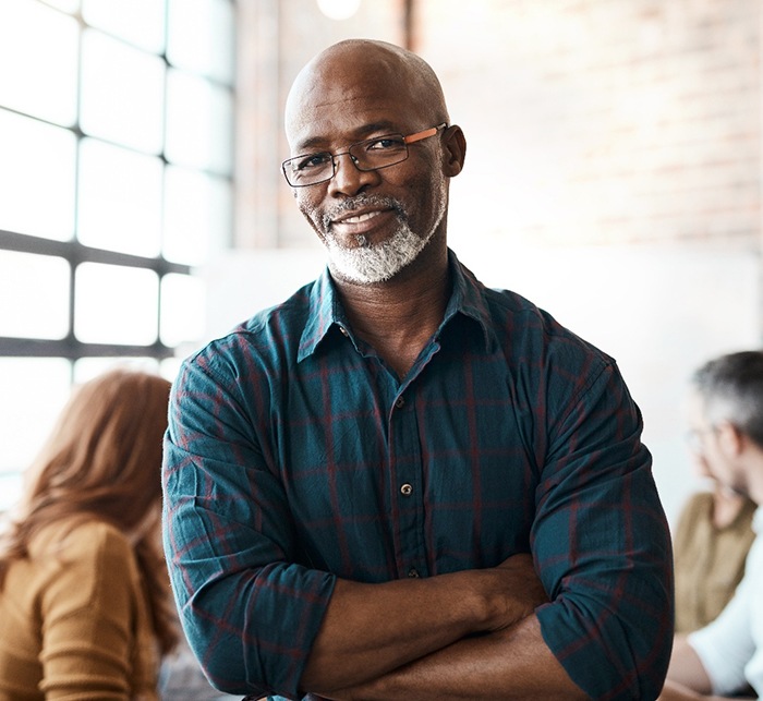 Man in brick room with arms crossed smiling
