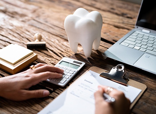 Patient calculating cost on desk with prop tooth