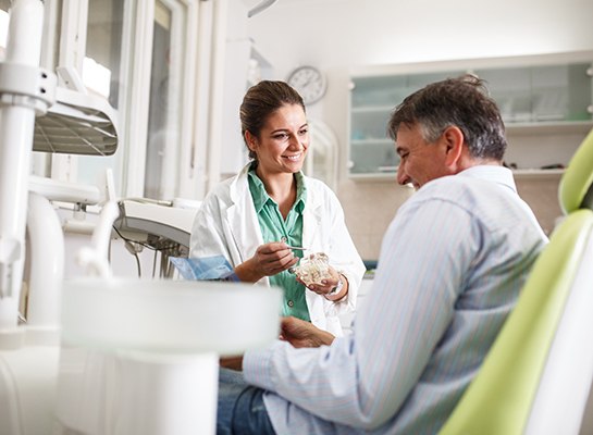 Smiling dentist showing patient model of teeth