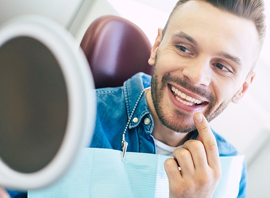 Man smiling at reflection in handheld mirror