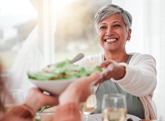 Smiling woman grabbing salad bowl across the table