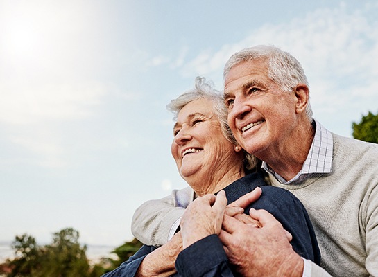 Senior couple smiling while hugging outside